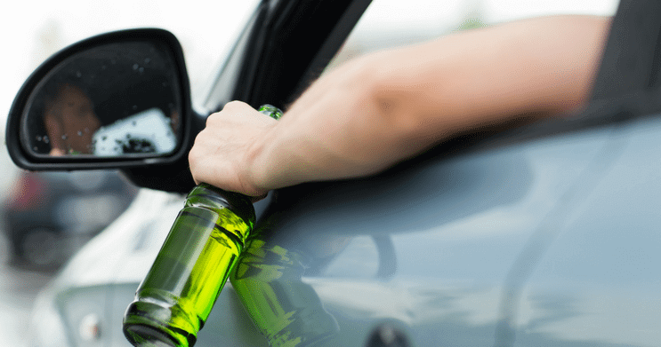 Man driving car while holding a liquor bottle out of his vehicle window