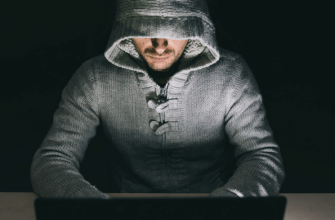 Man in a hooded sweatshirt sitting in front of a laptop computer in a dark room